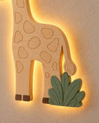 ORAWOOD giraffe wall-light 26x35 display detail 2026-09-28 5/5 — Lampe Girafe murale, mise en scène illustrative : Gros plan illustratif de la queue, de l’herbe vert sauge et du halo arrière